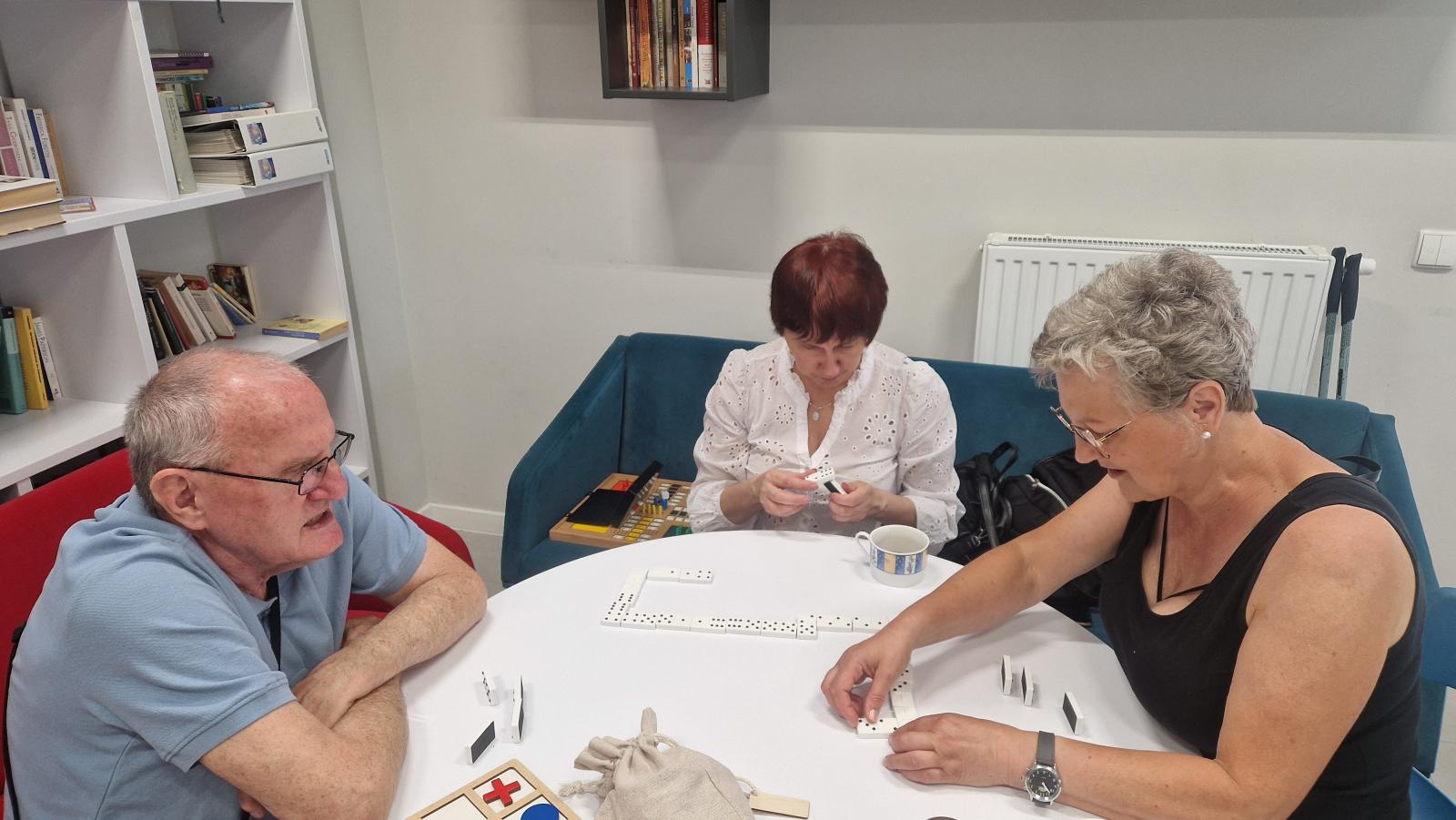 Dwie kobiety i jeden mężczyzna grają przy okrągłym stoliku w domino dotykowe