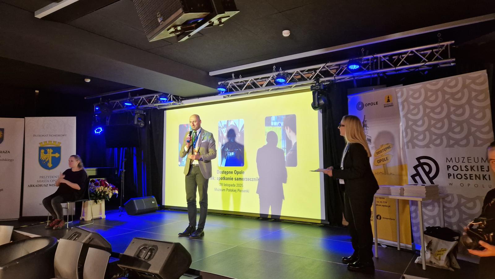 Na scenie Pan Łukasz Sowada, Zastępca Prezydenta Miatsa Opola, przemawia do mikrofonu.