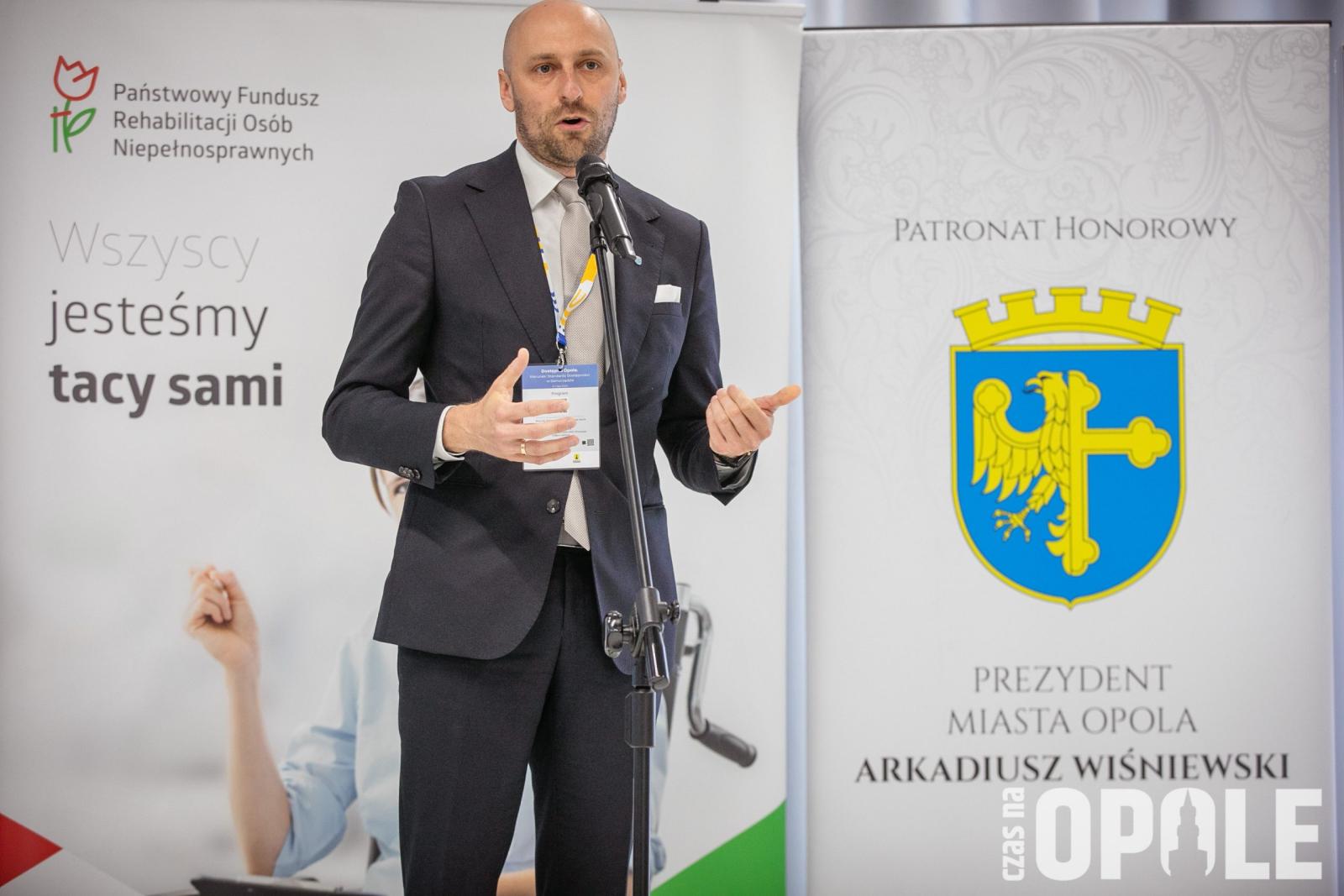 biały mężczyzna stojąc przy mikrofonie prfzemawia