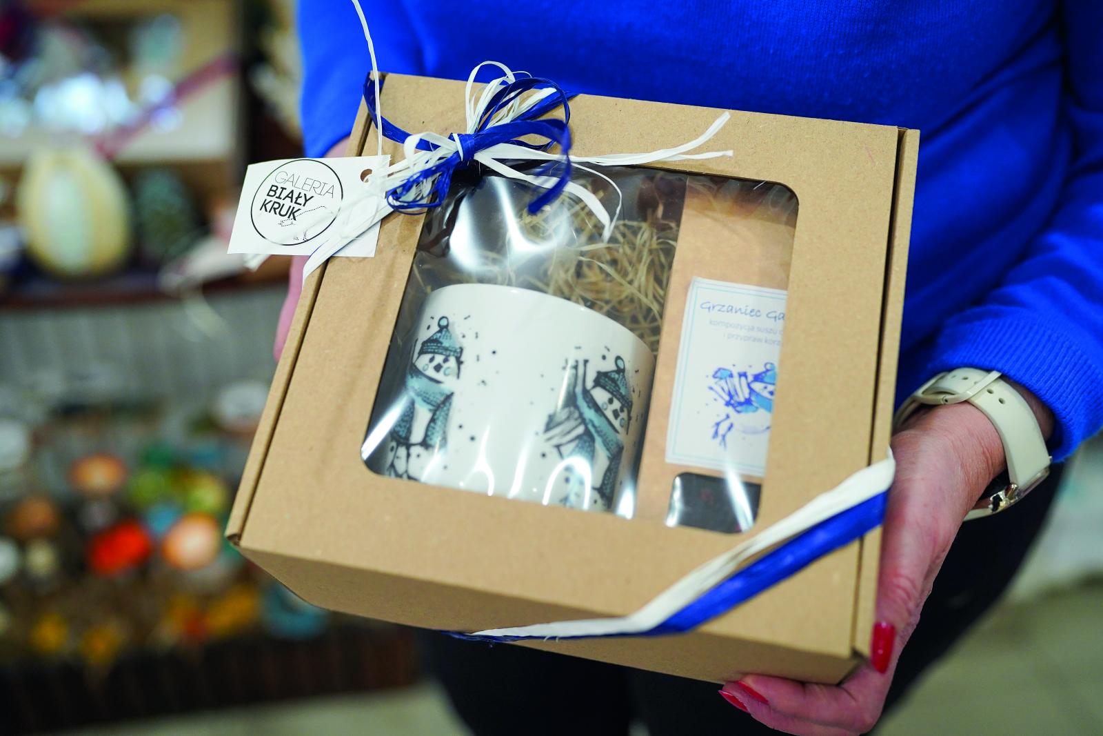 zdjęcie dłoni trzymających zestaw prezentowy w kartoniku zawiązanym wstążką
