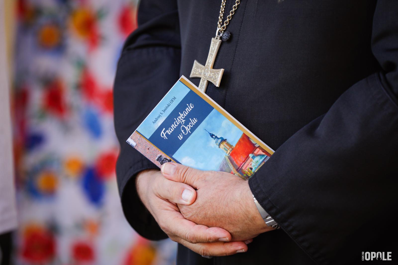 zdjęcie księdza trzymającego broszurę z napisem Franciszkanie w Opolu