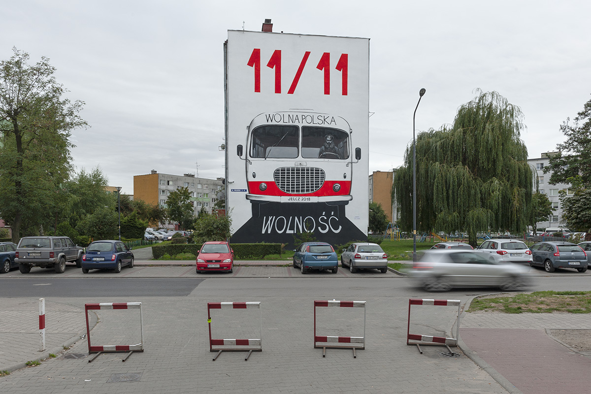 zdjęcie przedstawiające mural na budynku, na muralu znajduje się autobus z wyznaczonym kierunkiem "Wolna Polska", na drodze widnieje napis "wolność" a na górze muralu wielkie czerwone cyfry 11/11