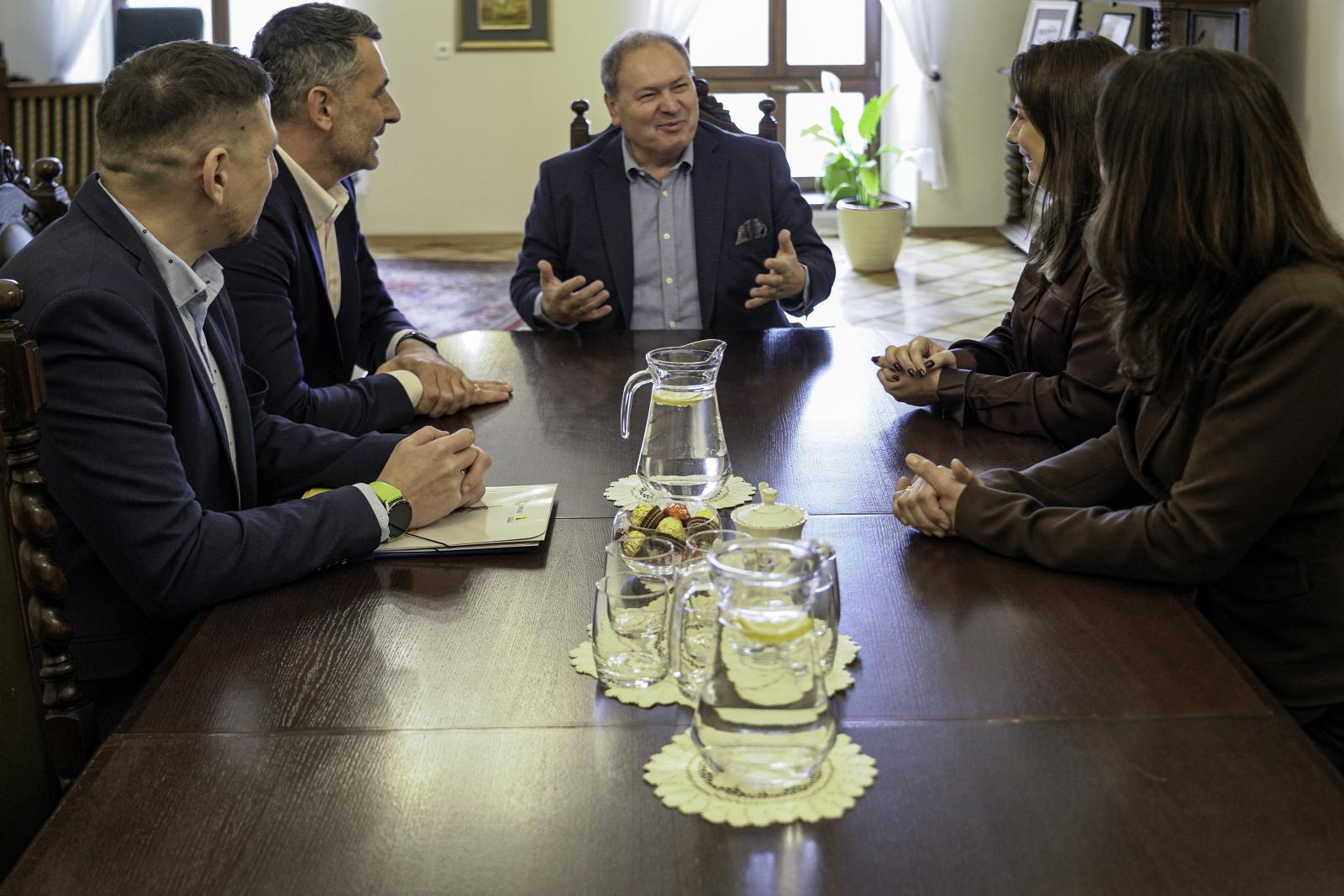 Grupa pięciu osób siedzi przy stole i rozmawia (trzech mężczyzn i dwie kobiety).