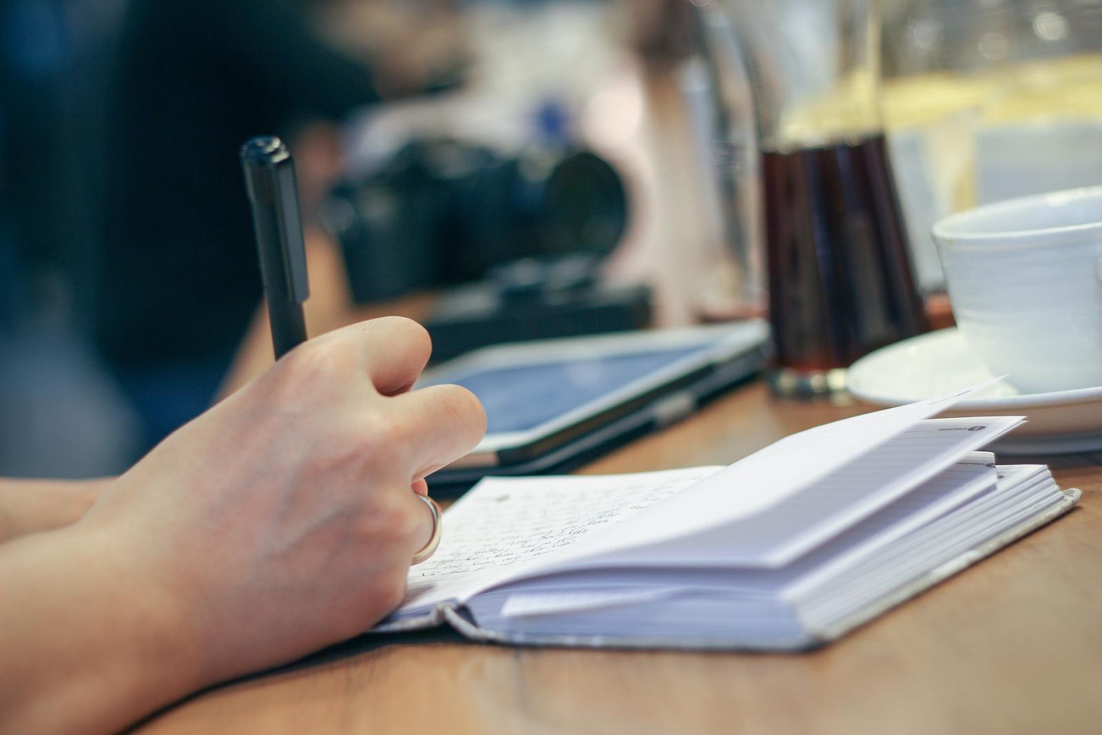 Dłoń trzymajaca długopis, nad białym notesem