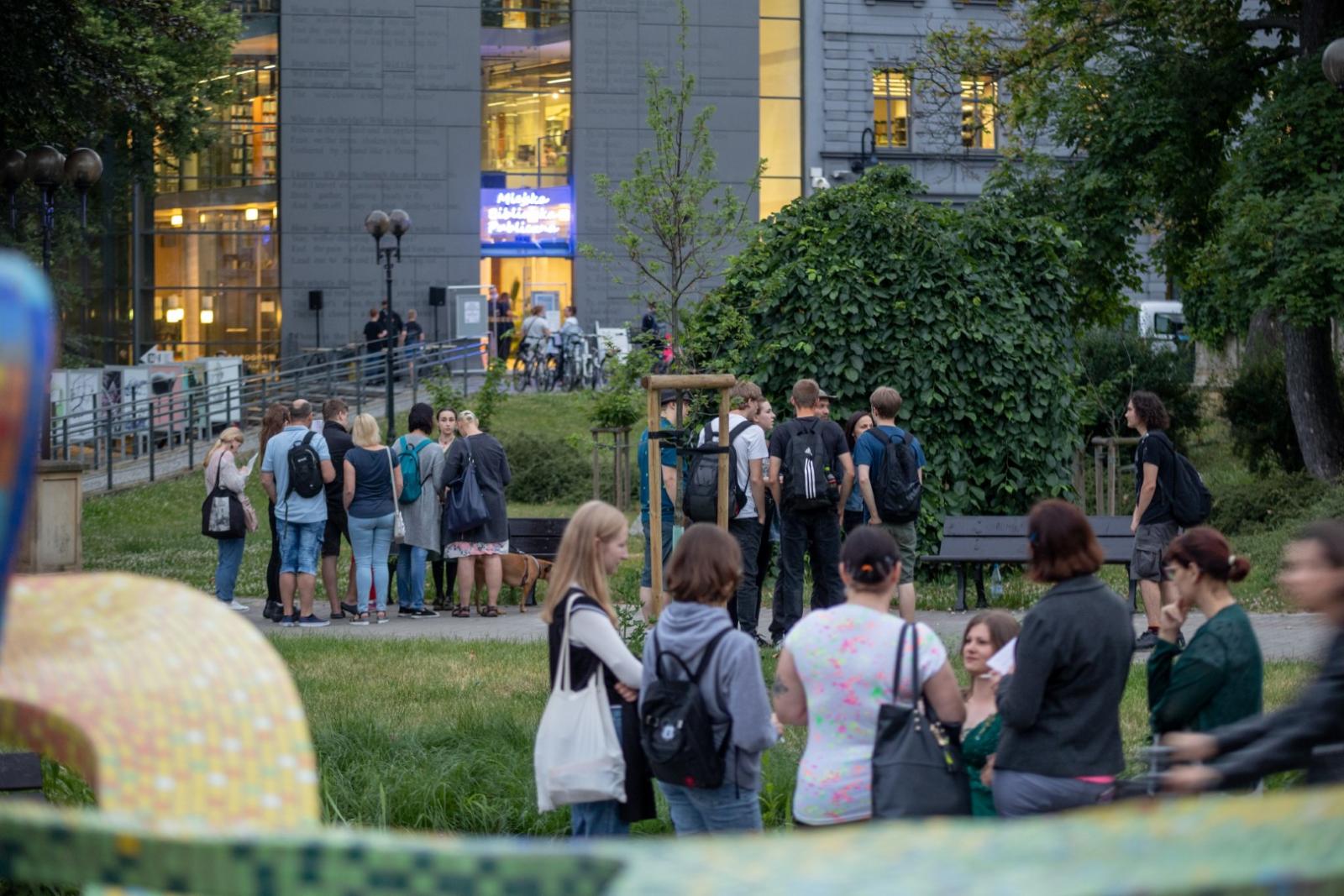 zdjęcie przedstawia budynek Miejskiej Biblioteki Publicznej oraz uczestników stojących przed fontanną, informacje zostały zawarte w tekście