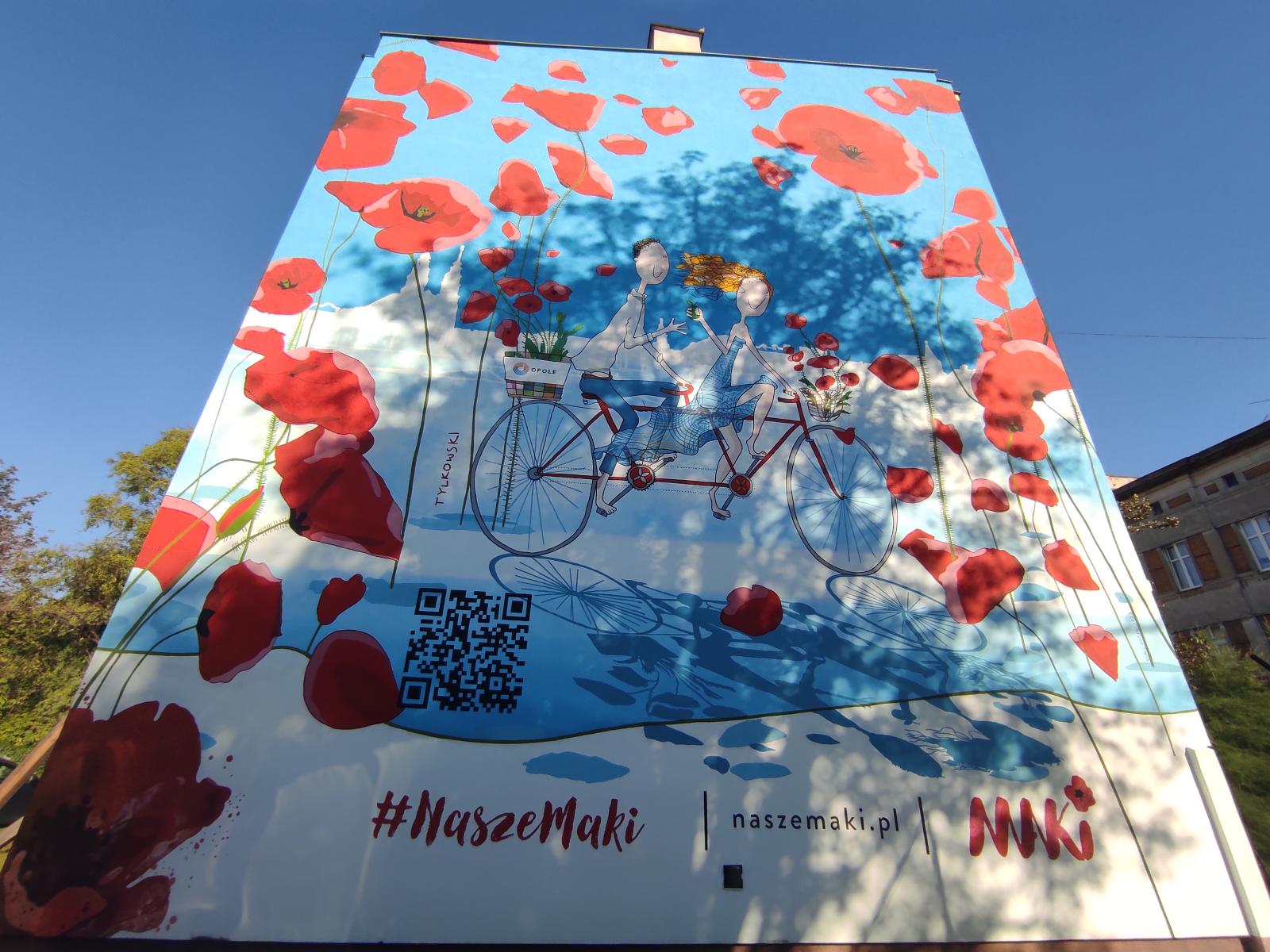 Mural przedstawiający mężczyznę i kobietę jadących na rowerze w tle maki