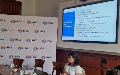 Prowadząca szkolenie p. Jadwiga Kost siedzi na krześle przed laptopem, za nią ekran z prezentacją Jak napisać tekst alternatywny?