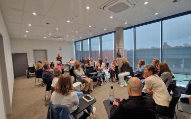 Szkolenie w sali, grupa ludzi siedząca na krzesłach i słucha osoby prowadzącej Alicję Stelmaszczy