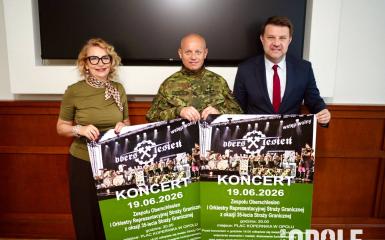 biala kobieta i dwóch białych mężczyzn, trzymaja plakaty informujące o wydarzeniu