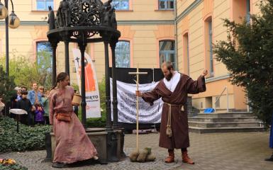 biała kobieta i biały mężczyzna, jako aktorzy, występują obok studni na Wzgórzu Uniwersyteckim podczas wydarzenia pt. Święto Wojciechowe