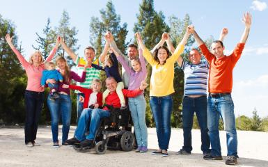 grupa osób, w tym osoba na wózku inwalidzkim, tyrzymającę ręce skierowane ku górze