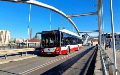 Most na rzeką. Na moście autobus. W tle wysokie bloki z wielkiej płyty. Pogodny dzień.