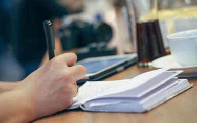 Dłoń trzymajaca długopis, nad białym notesem