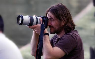 długowłosy mężczyzna robiący zdjęcie z użyciem aparatu fotograficznego z wysunietym obiektywem