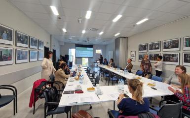 Grupa ludzi siedzących przy stołach podczas spotkania w sali Centrum Aktywizacji Społecznej. 