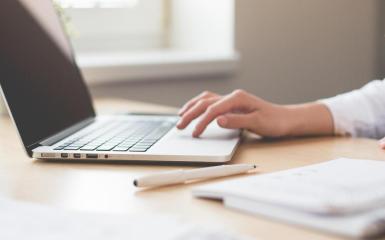 Zdjęcie przedstawia osobę piszącą na klawiaturze laptopa