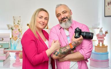 Para. Właściciele restauracji. Urbrani na różowo. Ona trzyma go pod ramię. On trzyma w dłoni aparat fotograficzny