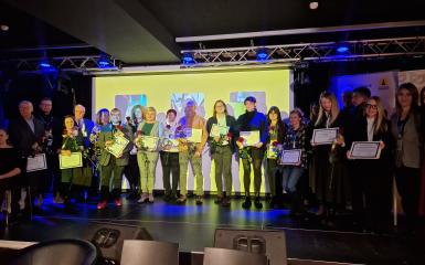 Zdjęcie grupowe uczetsników na scenie z dyplomami i różami.