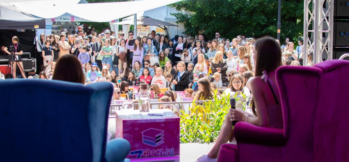 Osoby siedzące tyłem na scenie, przed nimi tłum ludzi