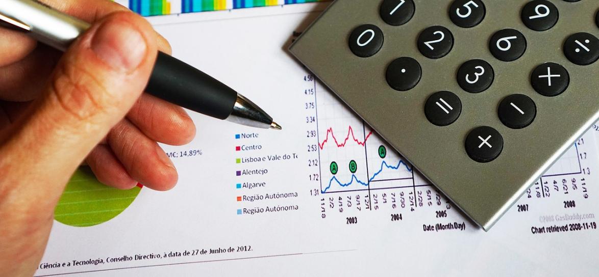 Dłoń trzymająca długopis, pod nią karta i kalkulator