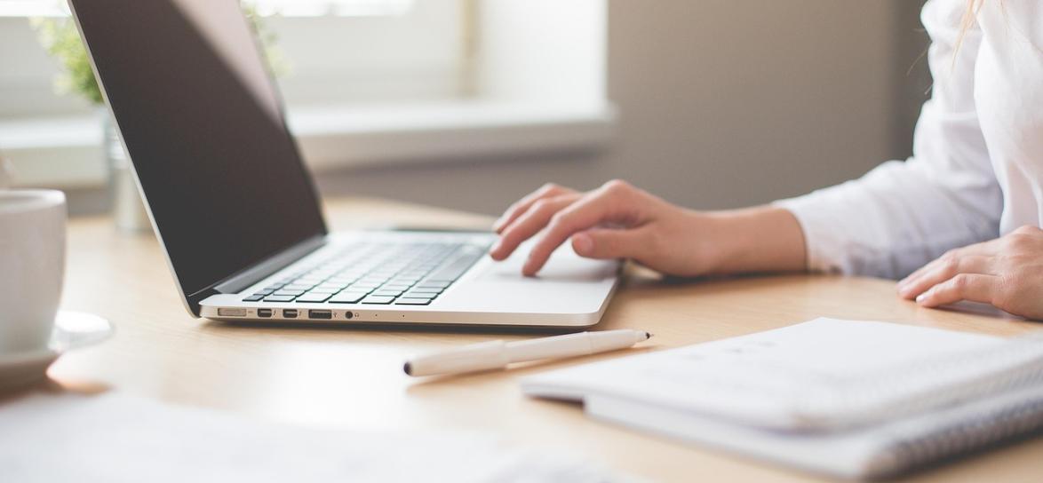 Zdjęcie przedstawia osobę piszącą na klawiaturze laptopa
