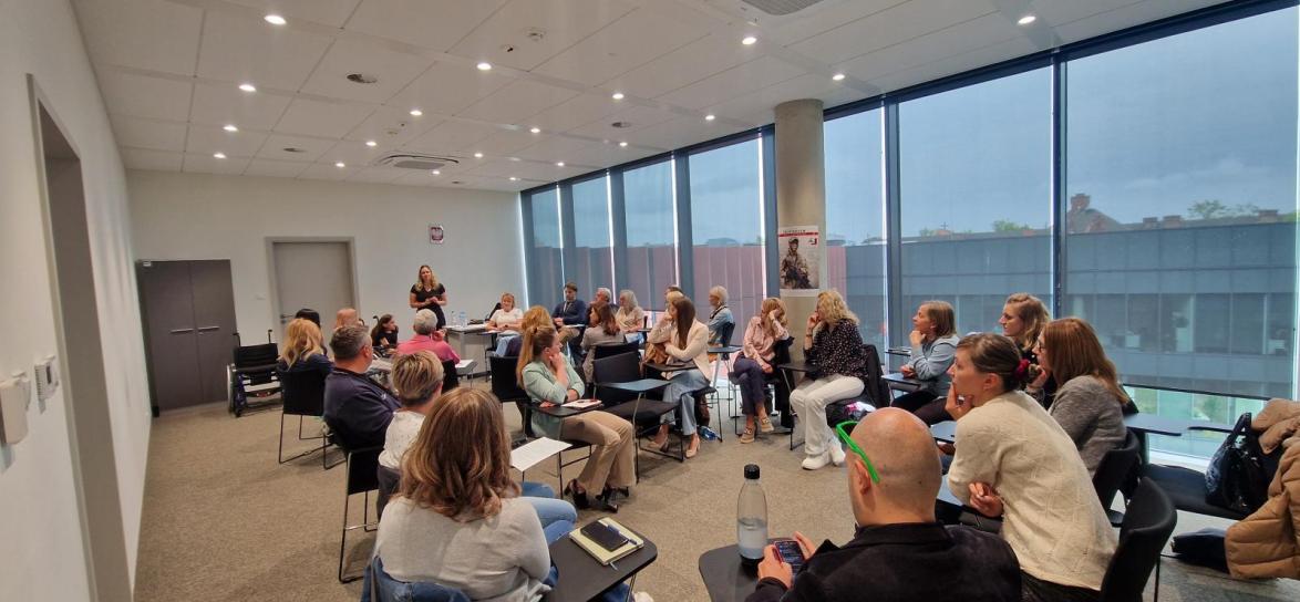 Szkolenie w sali, grupa ludzi siedząca na krzesłach i słucha osoby prowadzącej Alicję Stelmaszczy