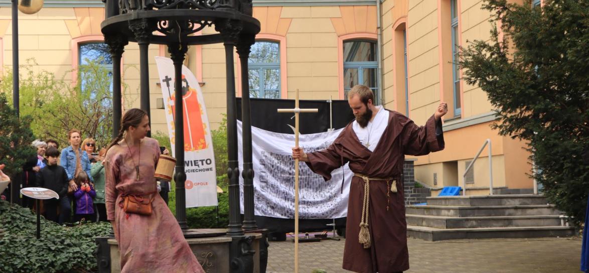 biała kobieta i biały mężczyzna, jako aktorzy, występują obok studni na Wzgórzu Uniwersyteckim podczas wydarzenia pt. Święto Wojciechowe