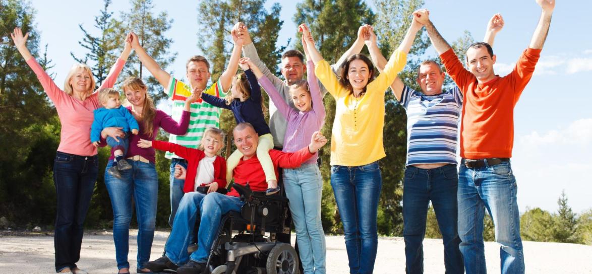 grupa osób, w tym osoba na wózku inwalidzkim, tyrzymającę ręce skierowane ku górze