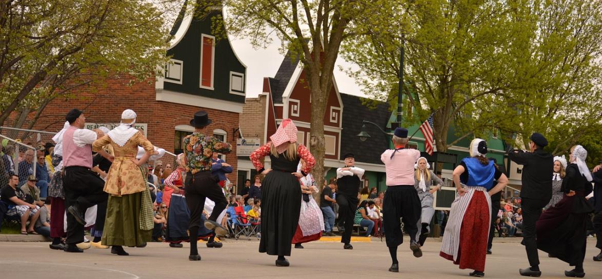zdjęcie przedstawia osoby tańczące na ulicy, w tym kobiety i mężczyżni, w strojach ludowych