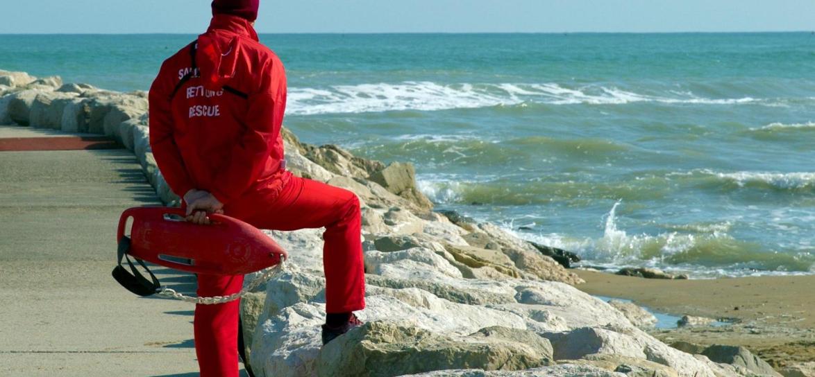 osoba stojąca nad brzegiem morza w czerwonym ubraniu