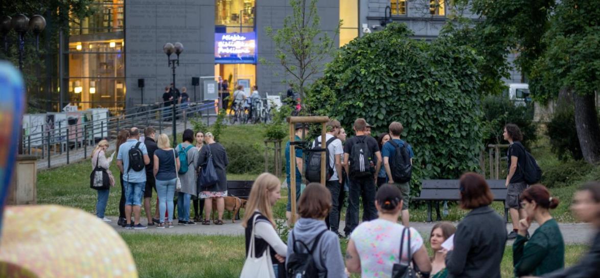 zdjęcie przedstawia budynek Miejskiej Biblioteki Publicznej oraz uczestników stojących przed fontanną, informacje zostały zawarte w tekście