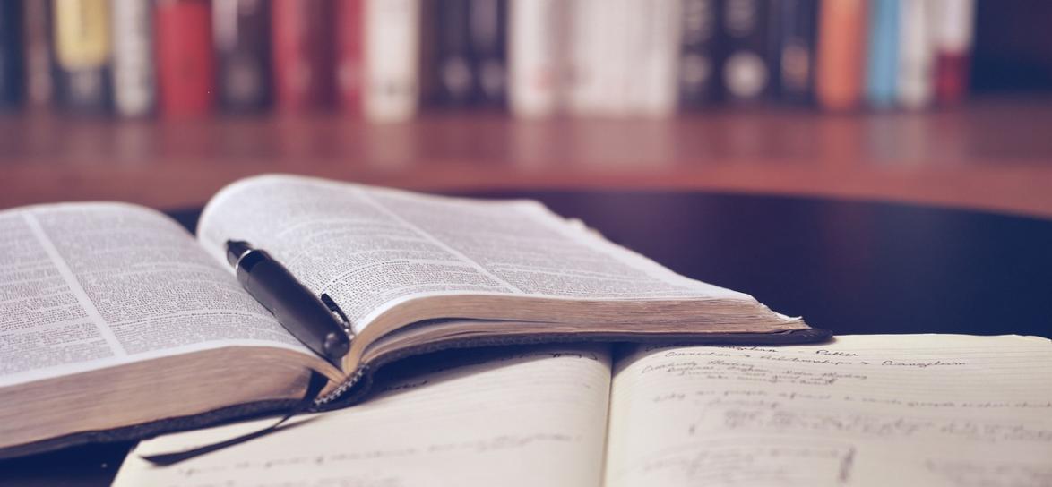 zdjęcie przedstawia otwarte książki na biurku, na jednej położny jest długopis