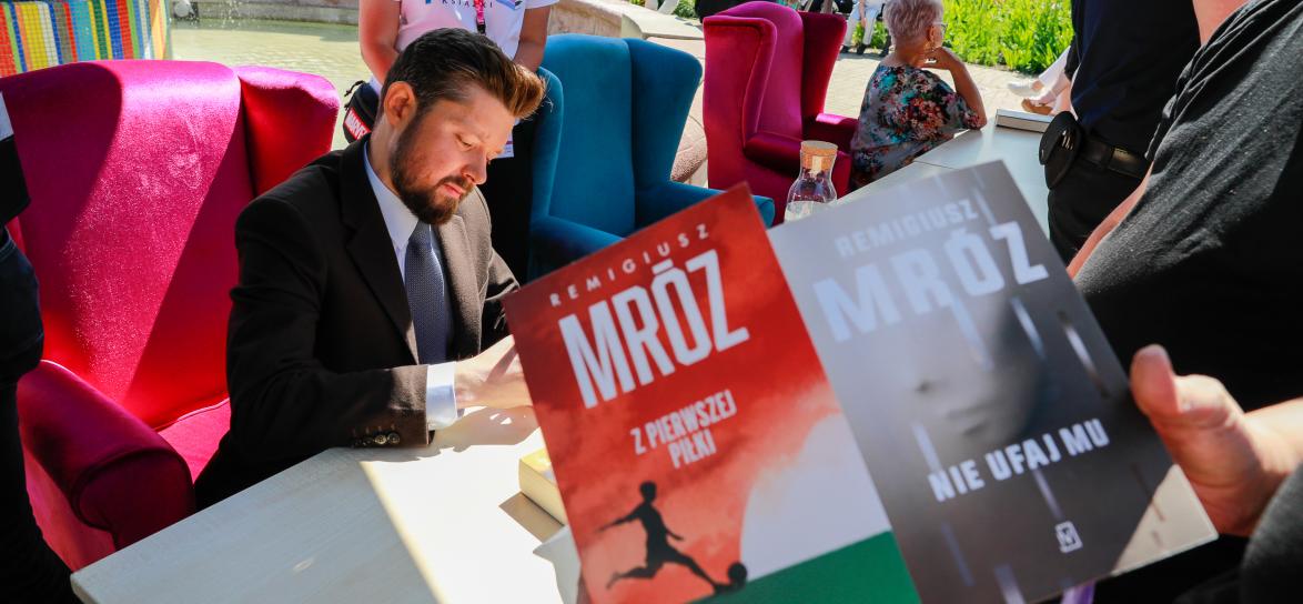 autor podpisuje autografy, mężczyzna, na ppierwszym planie okładka ksiązki
