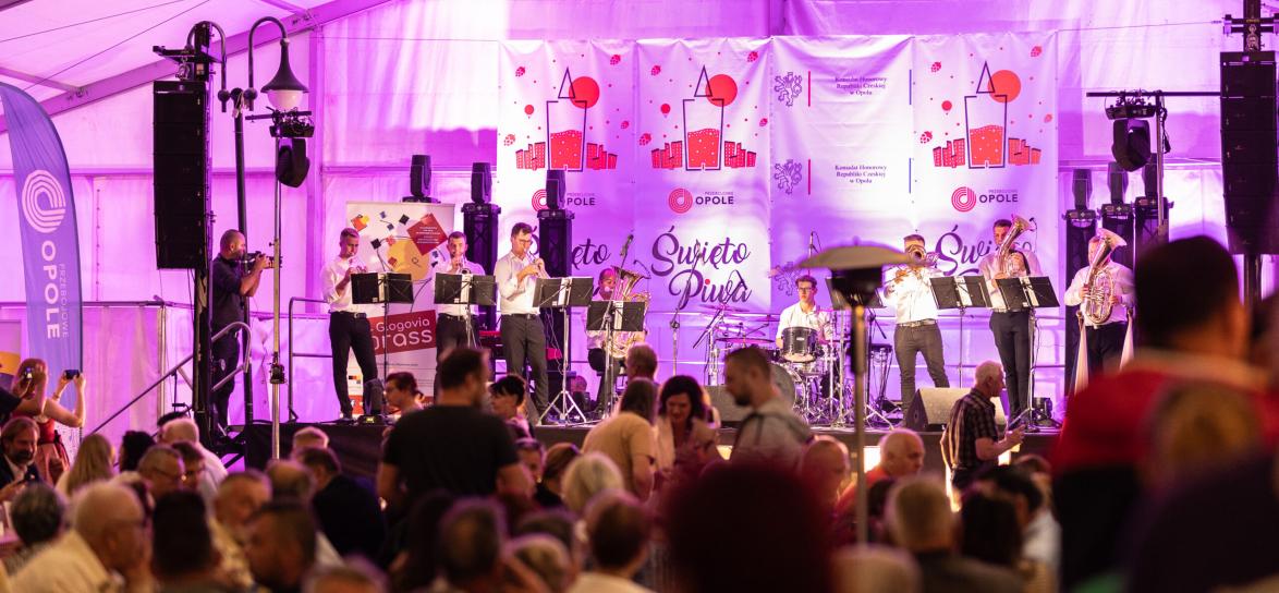 Duża grupa ludzi pod namiotem. Widok na scenę. Meżczyzna grający na istrumencie. Świeto Piwa