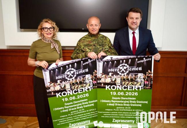 biala kobieta i dwóch białych mężczyzn, trzymaja plakaty informujące o wydarzeniu