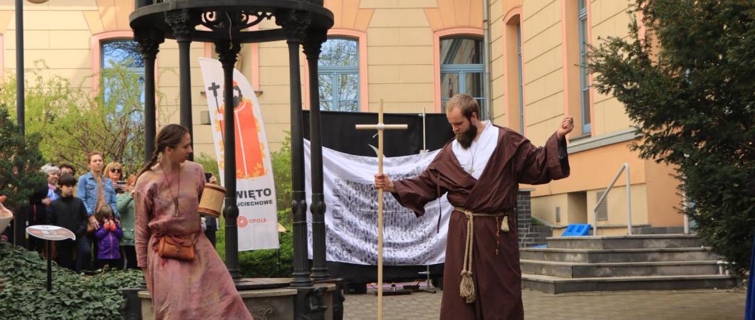 biała kobieta i biały mężczyzna, jako aktorzy, występują obok studni na Wzgórzu Uniwersyteckim podczas wydarzenia pt. Święto Wojciechowe