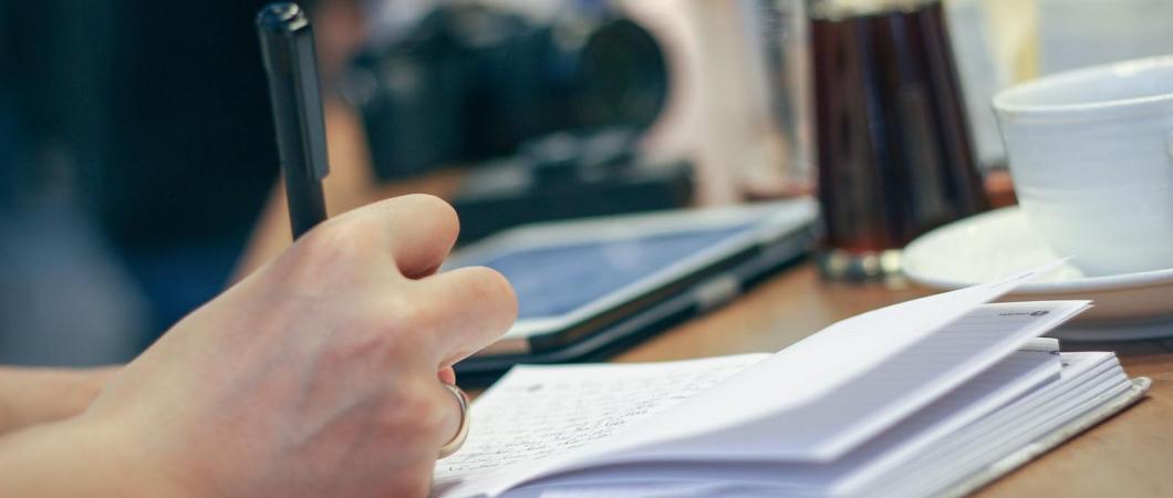 Dłoń trzymajaca długopis, nad białym notesem