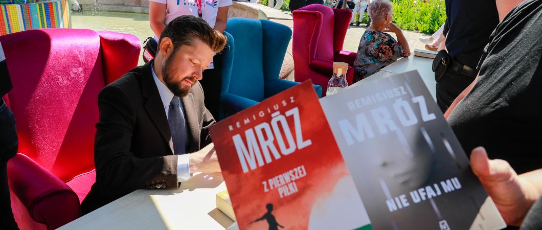 autor podpisuje autografy, mężczyzna, na ppierwszym planie okładka ksiązki