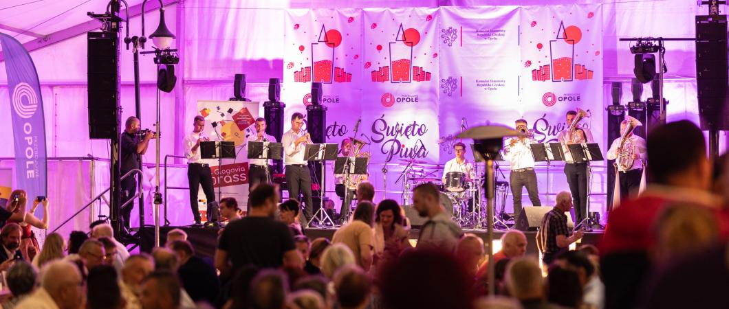 Duża grupa ludzi pod namiotem. Widok na scenę. Meżczyzna grający na istrumencie. Świeto Piwa