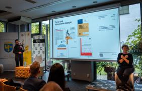 Wyświetlający się slajd z napisem "To nie jest odkrywanei Ameryki", po lewej stronie kobieta przemawia do mikrofonu, po prawej siedzi tłumacz języka migowego