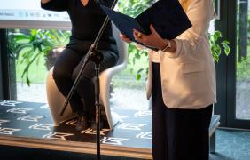 przemawiająca do mikrofonu kobieta, w oddali tłumacz języka migowego