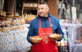zdjęcie przedstawiające mężczyznę częstującego chlebem - w tle stoisko