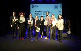 zdjęcie grupowe laureatów nagród w kulturze, którzy stoją na scenie, w tle prezentacja