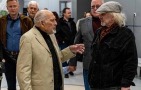 dwóch dojrzałych męzczyzn rozmawia, wernisaż wystawy, w tle inne osoby